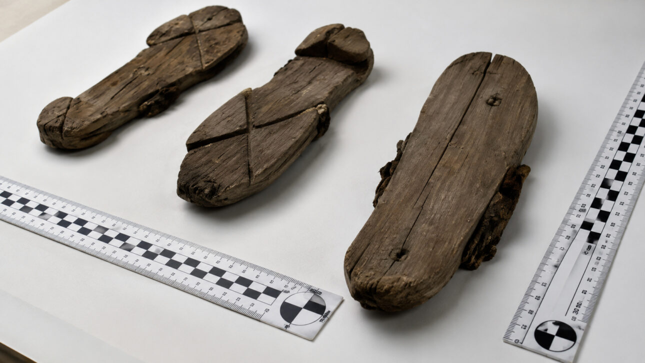 Tamancos romanos de madeira preservados em mesa de análise arqueológica, ao lado de réguas de medição.