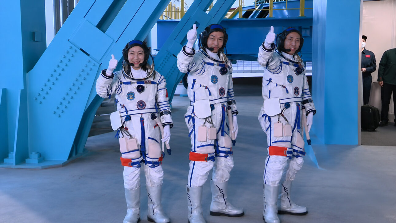Three Chinese astronauts in spacesuits give a thumbs-up during preparation for the Shenzhou-23 mission.