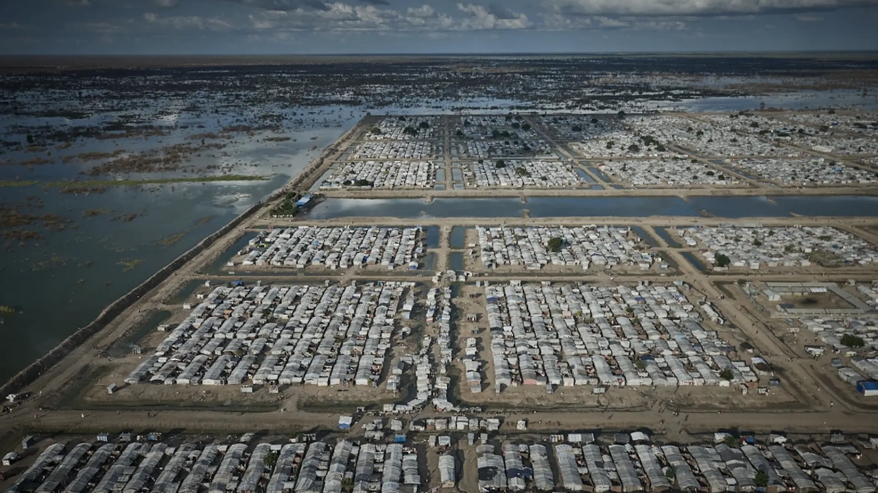Vista aérea do campo de Bentiu, no Sudão do Sul, cercado por áreas alagadas e canais de contenção, onde milhares de famílias deslocadas vivem em abrigos vulneráveis às enchentes. Fonte: Aerial view of Bentiu camp.