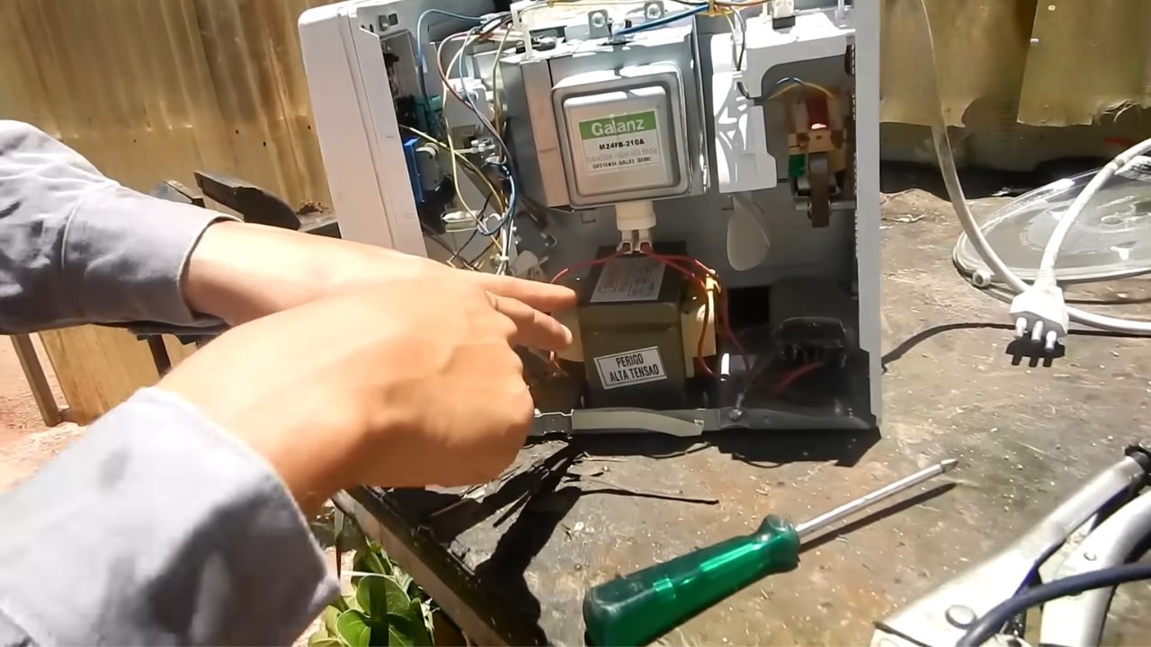 Micro-ondas aberto mostra o transformador interno reaproveitado no projeto de máquina de solda caseira, peça que virou o centro da adaptação feita com componentes retirados de aparelhos antigos. Fonte: LetraJota/Reprodução.