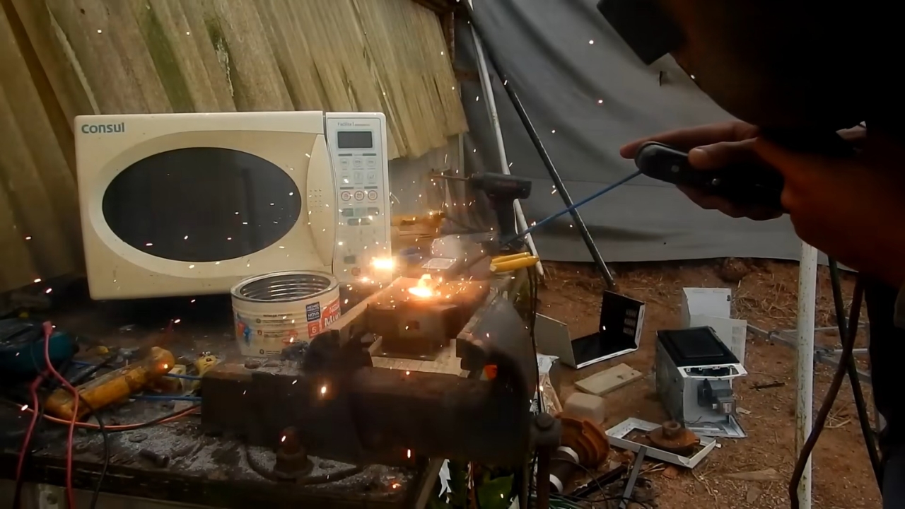 Máquina de solda caseira feita com transformadores reaproveitados de micro-ondas entra em funcionamento durante teste na bancada, soltando faíscas ao unir peças de metal. Fonte: LetraJota/Reprodução.