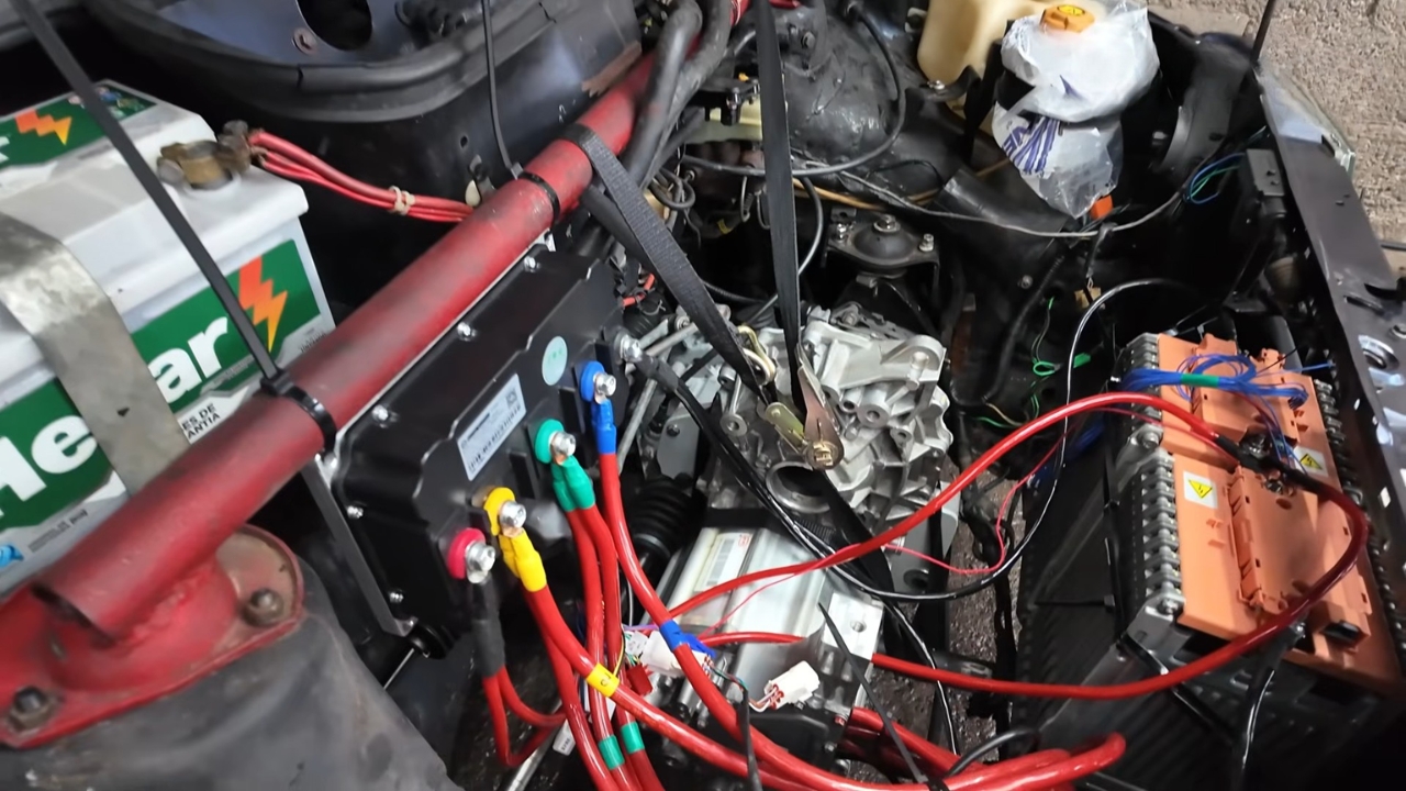 Compartimento do Fiat Uno mostra a adaptação elétrica ainda em fase de testes, com controladora, cabos de alta corrente, baterias e motor já instalados para fazer o carro rodar sem motor a combustão. Fonte: canal LetraJota/YouTube.