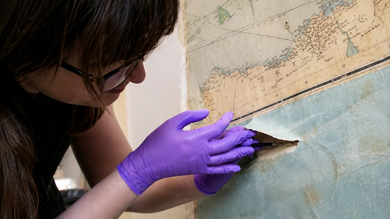 Conservators remove two layers of wallpaper from a depot in a palace and find 11 maps from the 1930s with erupting volcano, mythical creature, and travel scenes preserved after 1,600 hours of work