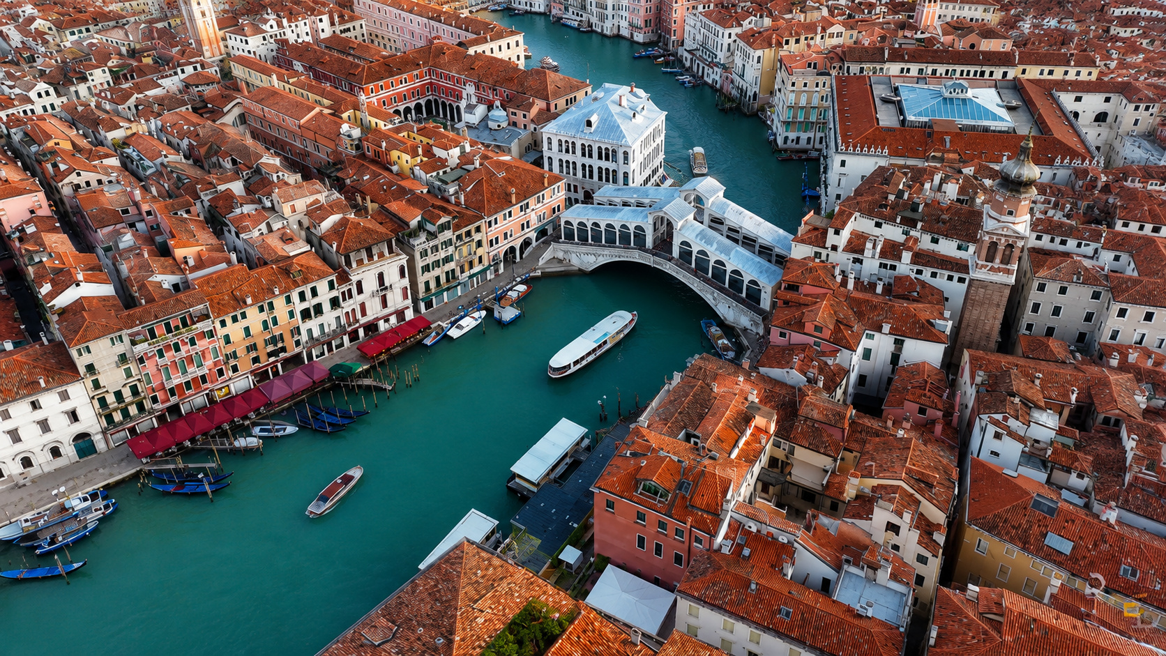 Vista aérea do Grande Canal de Veneza com a Ponte de Rialto, edifícios históricos, embarcações e a cidade construída sobre a água.