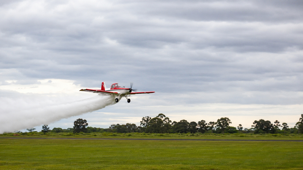 Avião agrícola sobrevoa área rural durante pulverização; o projeto prevê controle remoto pelo piloto no solo e futura operação totalmente autônoma.