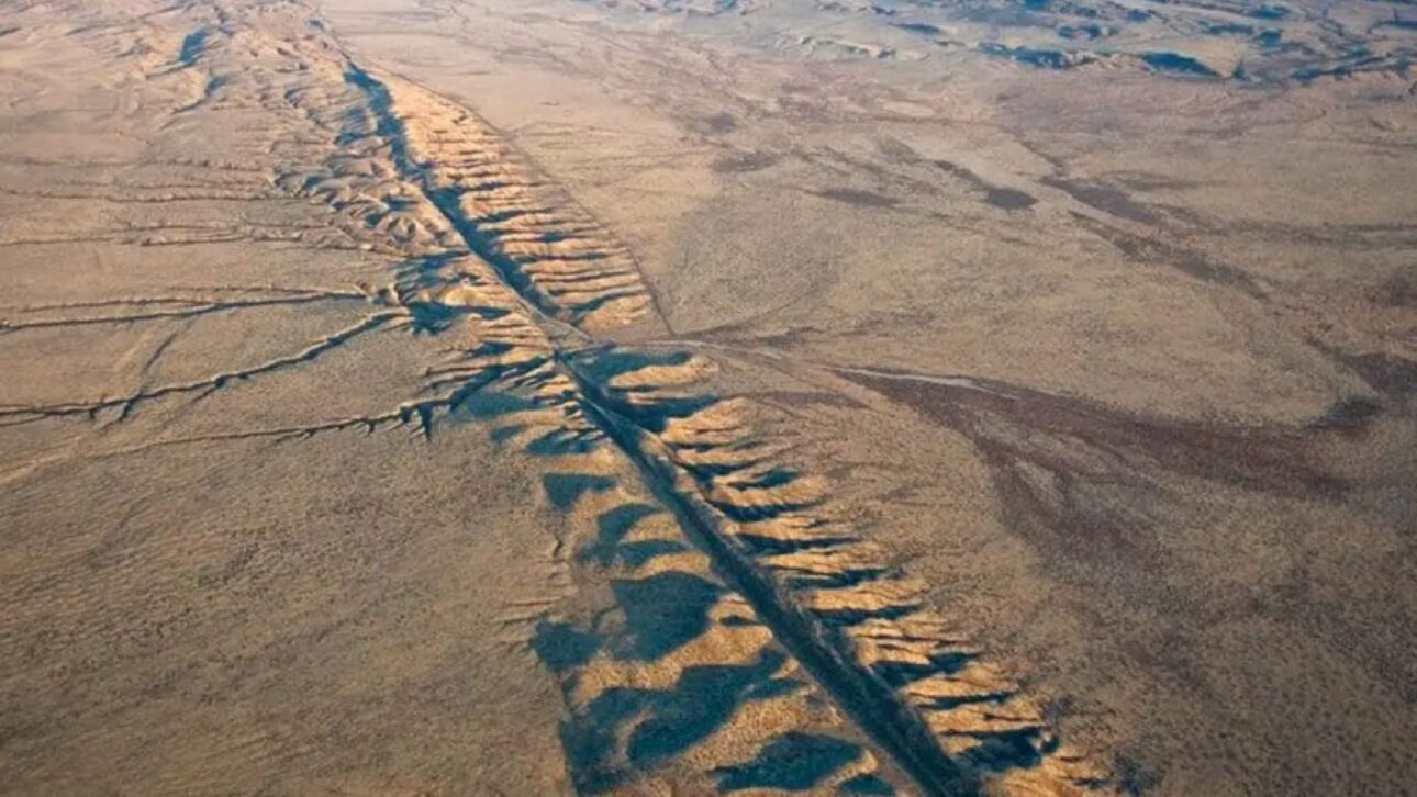 Vista aérea de línea de falla geológica cortando paisaje árido y rocoso de California bajo cielo claro