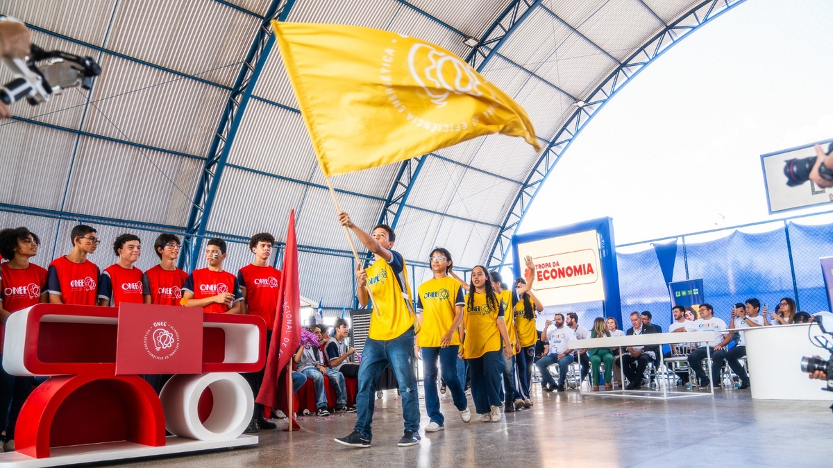 Estudantes com camisetas coloridas da ONEE participam de atividade educativa em quadra coberta durante a Olimpíada Nacional de Eficiência Energética.