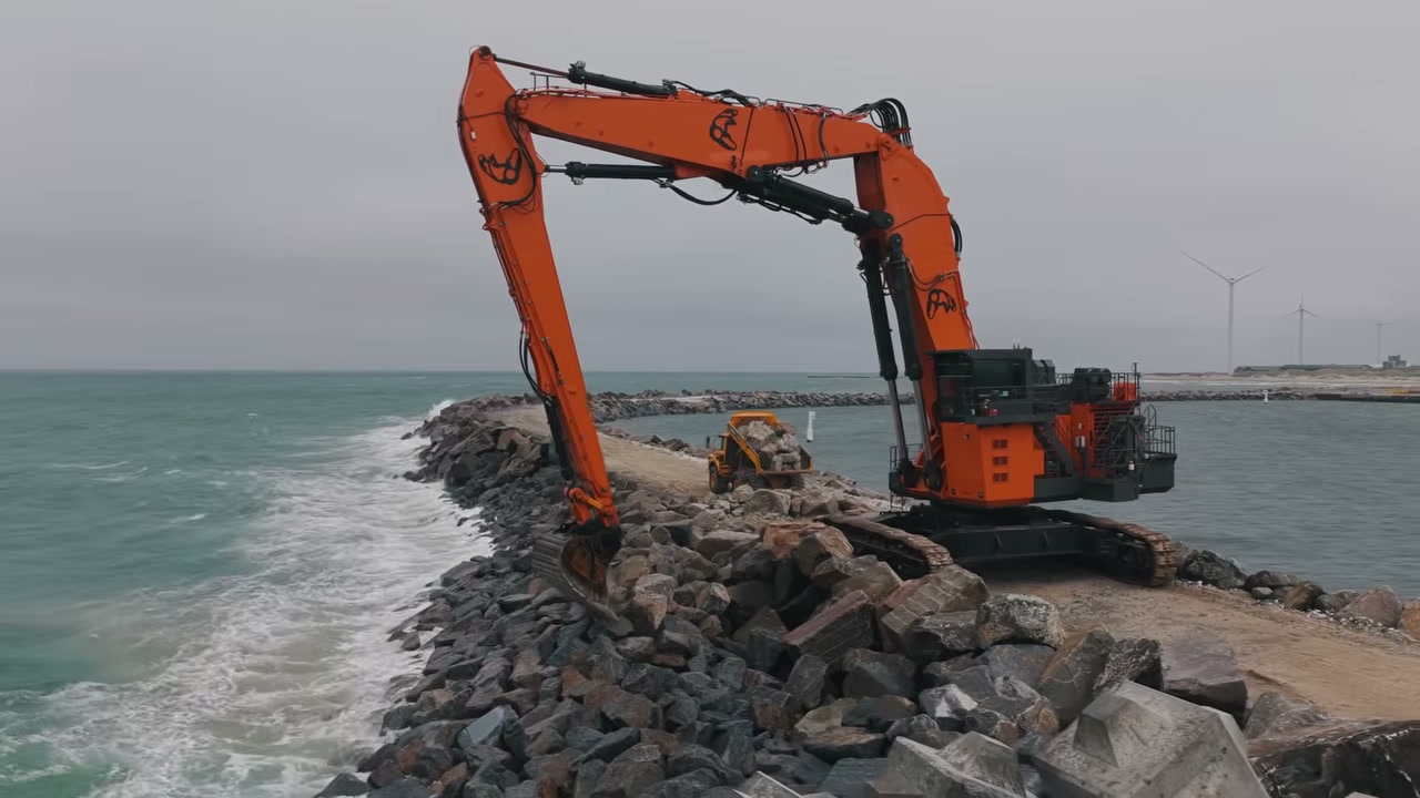 The gigantic triple boom excavator working on the breakwater, with the boom extended over the sea, the scene that earned the project the nickname "wall in the ocean". Credit: Earthmovers Media (YouTube).