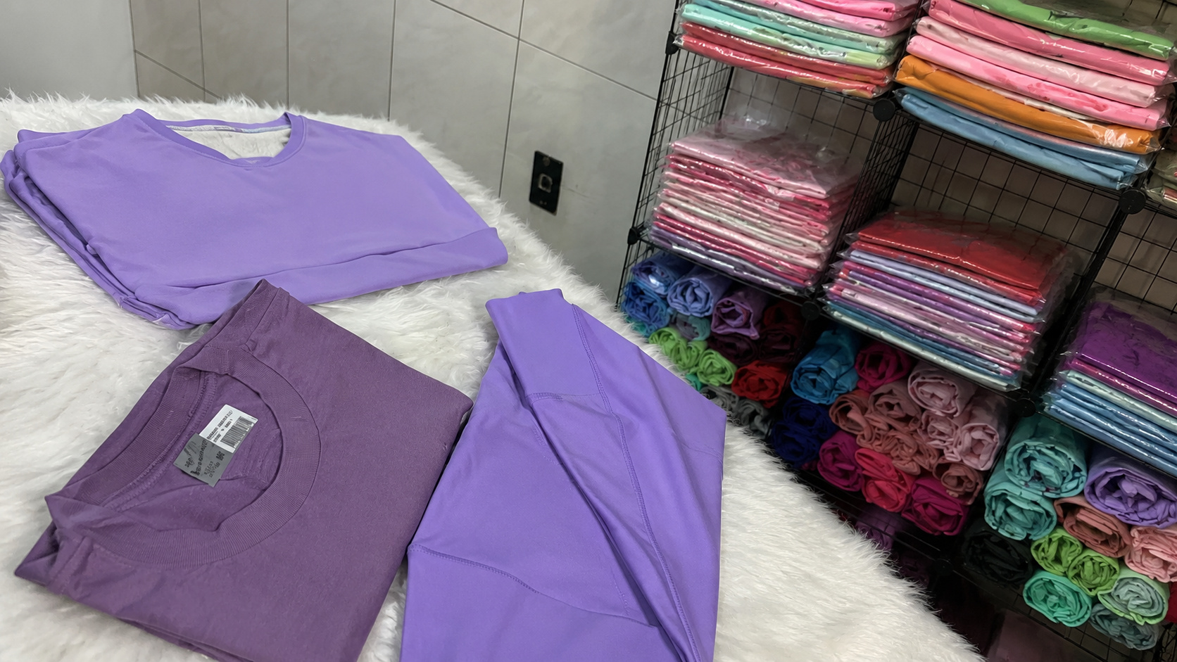 Roupas coloridas e peças roxas organizadas em loja especializada em moda penitenciária para visitantes de presídios.