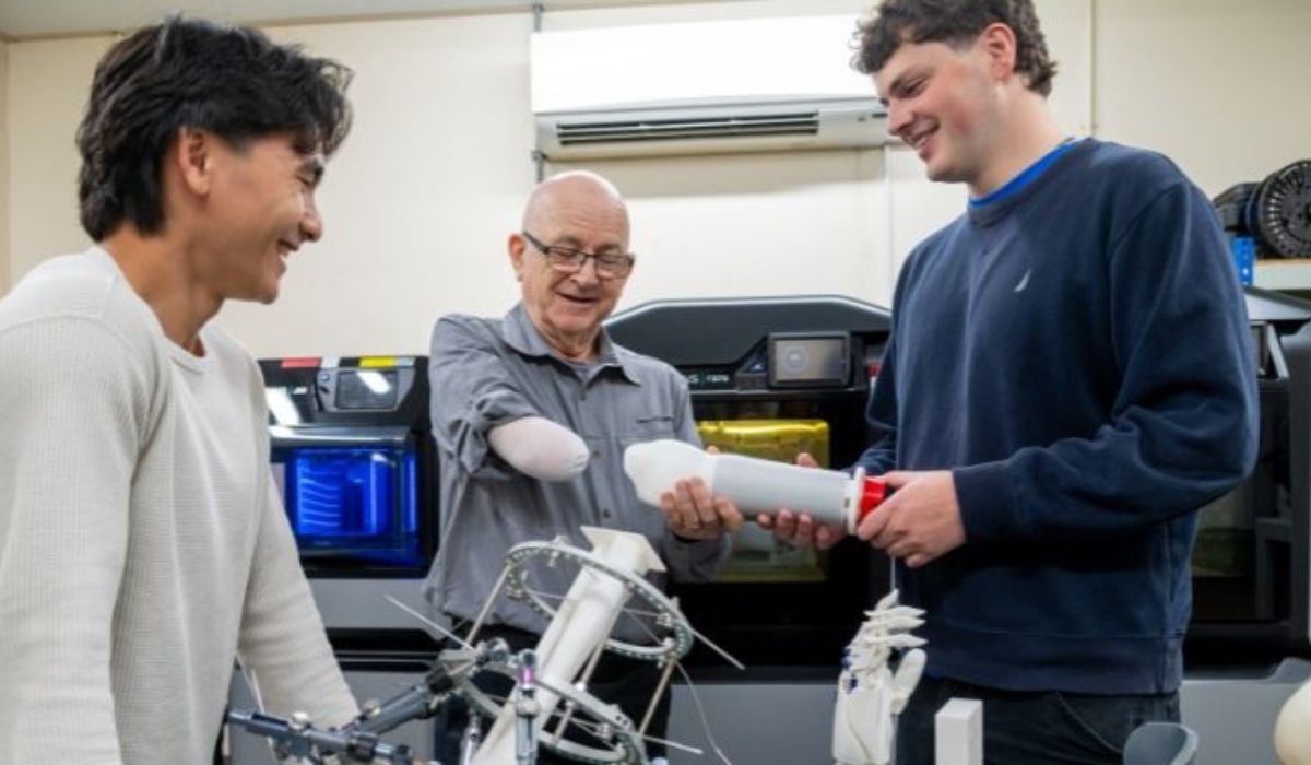 Os estudantes Hugo Wong e Teddy Strange apresentam a George Glasgow a prótese temporária produzida com impressão 3D e componentes modulares. Crédito: Mark Bickerdike/Universidade de Leeds.
