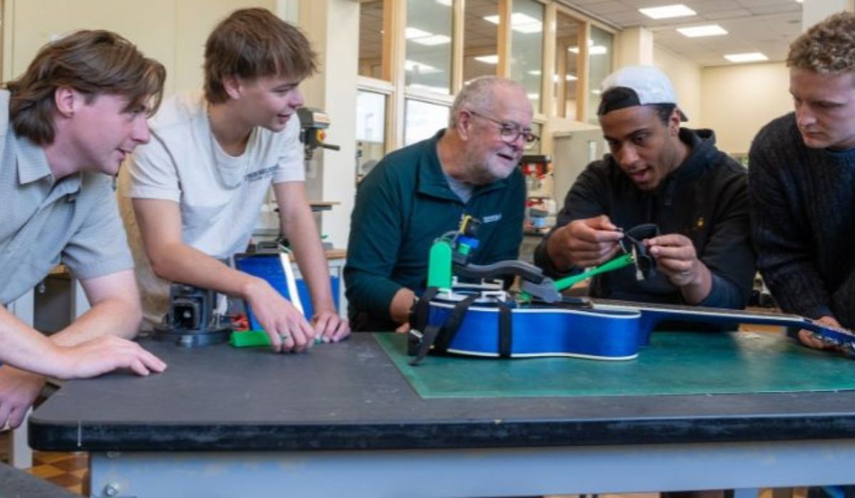 Harvey Roberts, Isaac Martin, Gerry Van Hee, Phil Asante-Siaw e Sam Matthews observam o dispositivo de assistência instalado em um violão durante o desenvolvimento do projeto. Crédito: Mark Bickerdike/Universidade de Leeds.