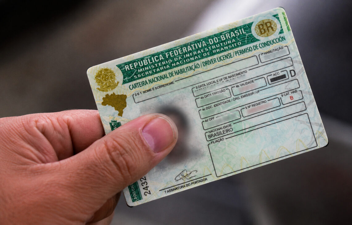 Mão segurando uma Carteira Nacional de Habilitação (CNH) brasileira, ilustrando proposta sobre suspensão da CNH por abandono de animais com veículo.