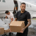 Neymar carrega caixa com donativos ao lado de jato particular durante ação ilustrativa de ajuda às vítimas das enchentes no Rio Grande do Sul.