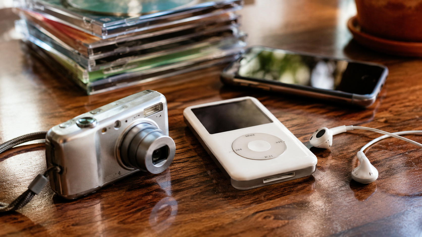Câmera digital, tocador de MP3 com fones de ouvido com fio e smartphone sobre mesa, representando tecnologias antigas que voltaram a conquistar jovens.