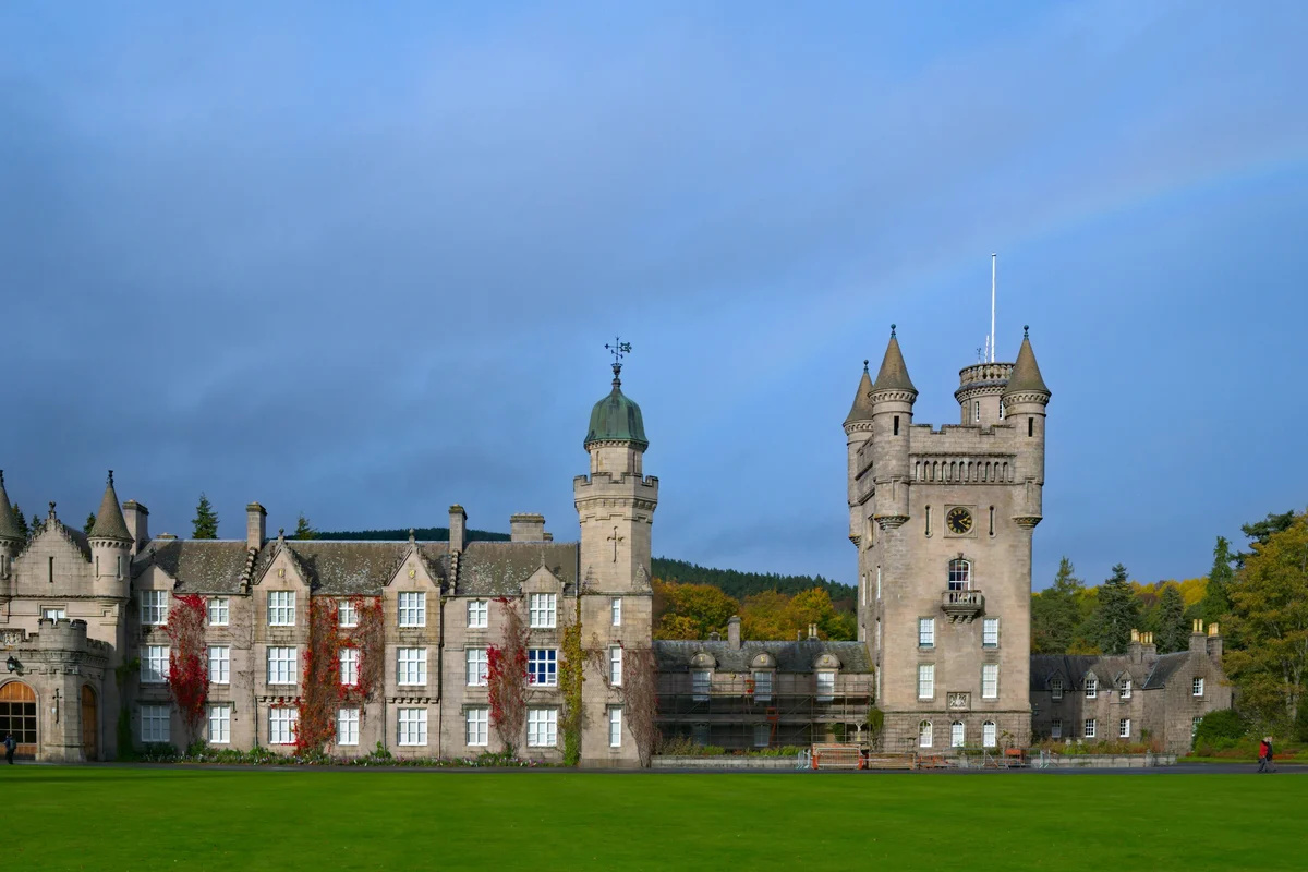 Fachada do castelo de Balmoral, na Escócia, com torre de relógio, hera avermelhada nas paredes e gramado vazio em primeiro plano