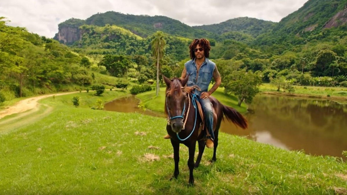 Lenny Kravitz montado a cavalo em área verde com lago e montanhas na fazenda em Duas Barras.