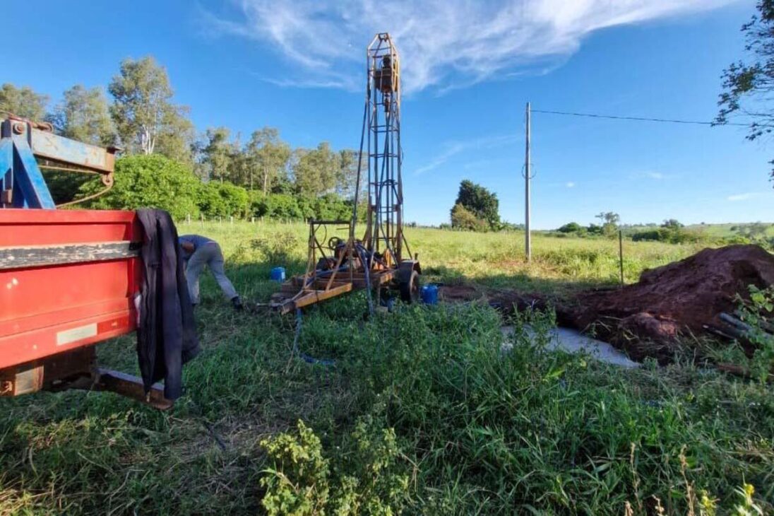 Estrutura usada para perfurar poço permanece instalada em área rural ao lado de caminhão e terra removida.