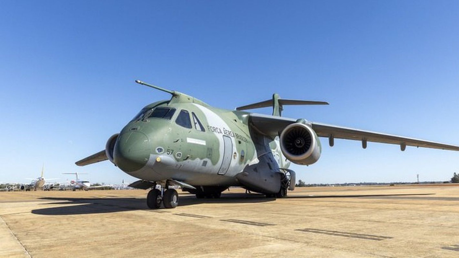 Avião militar de transporte verde e cinza, com a inscrição Força Aérea Brasileira na fuselagem, parado no pátio sob céu azul.